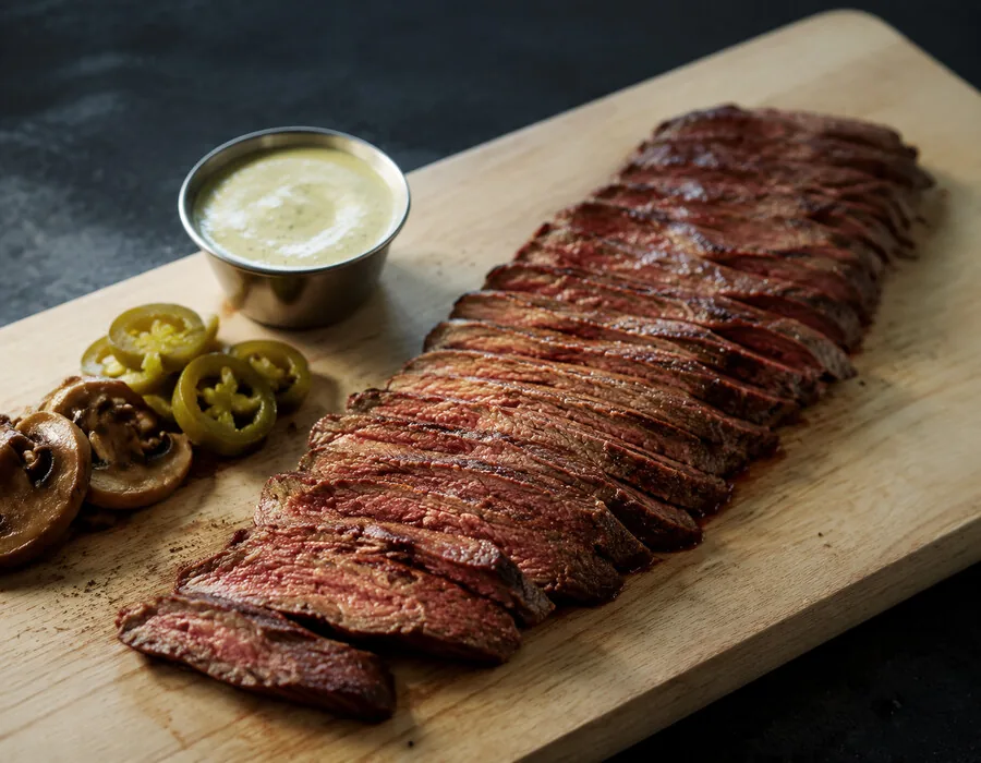 Aufgeschnittenes Flanksteak auf einem Holzbrett mit Dip