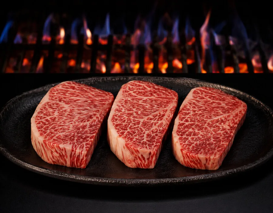 Drei marmorierte Steaks auf einer Gusseisenplatte am Grill